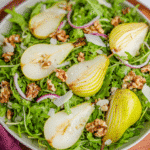 arugula pear salad on white platter with dressing