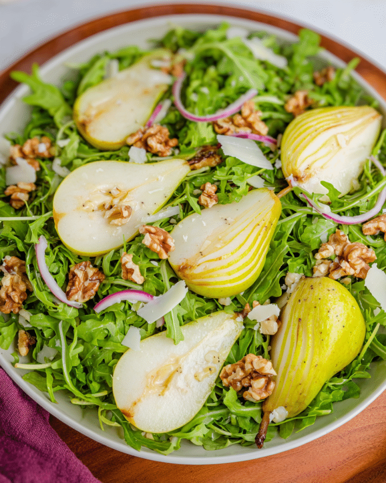 arugula pear salad on white platter with dressing