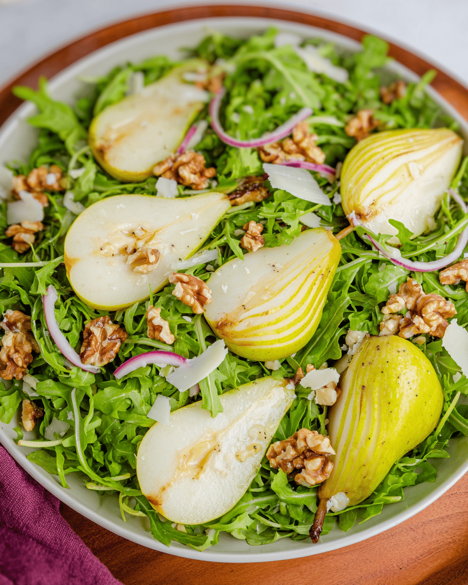 arugula pear salad on white platter with dressing