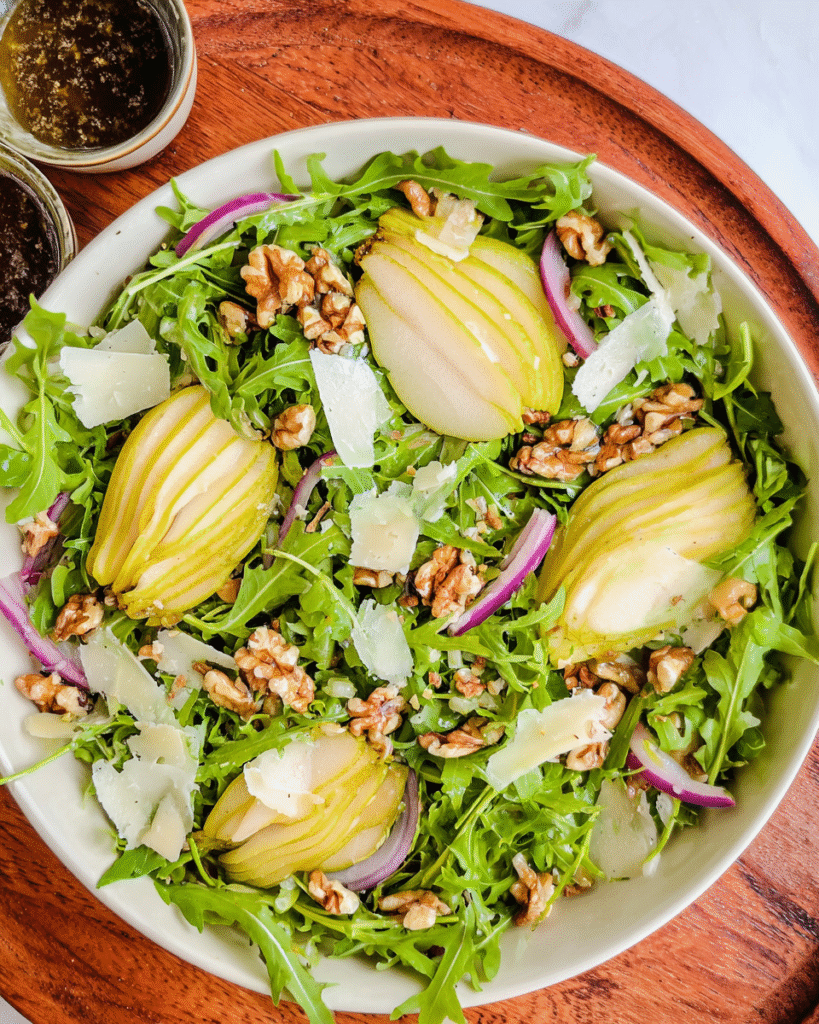 arugula pear salad on white platter with dressing