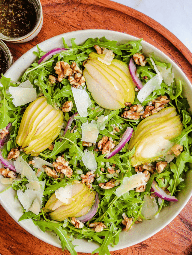 arugula pear salad on white platter with dressing