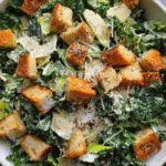 kale caesar salad in bowl with creamy dressing and croutons