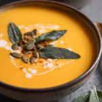 Bowl of apple butternut squash soup topped with crispy sage and pepitas