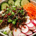 Korean-inspired ground beef bowl with rice, cucumbers, carrots, and sesame seeds